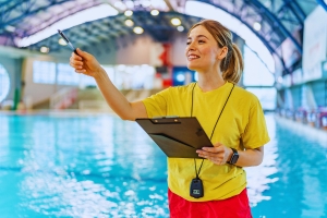 A lifeguard stands on the side of the pool blowing whistle