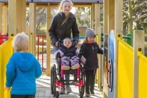 Children walk across a bridge on a playground. One is in a wheelchair.