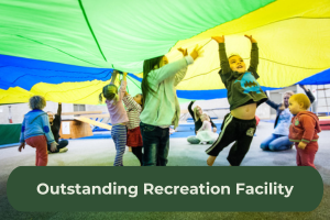 Children play under a rainbow parachute with the copy 'Outstanding Recreation Facility'