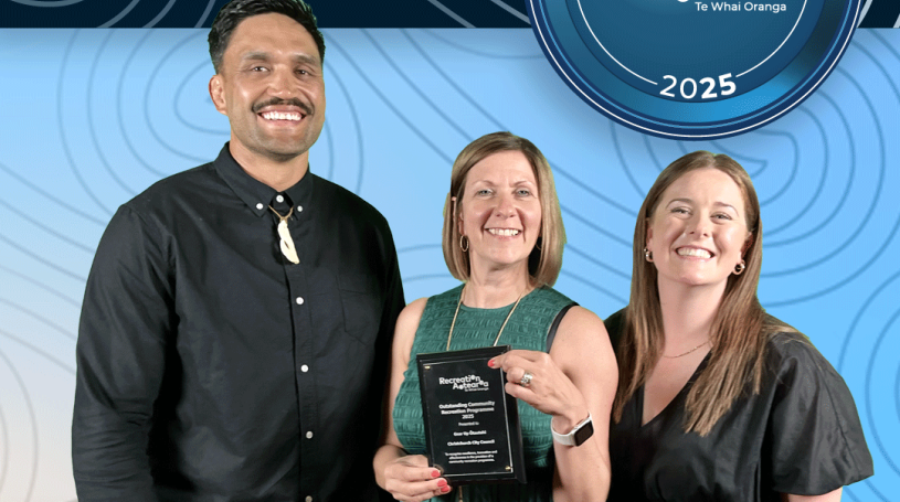 A man and two women standing together holding an award plaque and smiling. The background is a blue koru pattern with text at the top and bottom of the image. The top text says "2025 Recreation Awards Winner," and the bottom says "Outstanding Community Recreation Programme: Gear Up Ōtautahi"