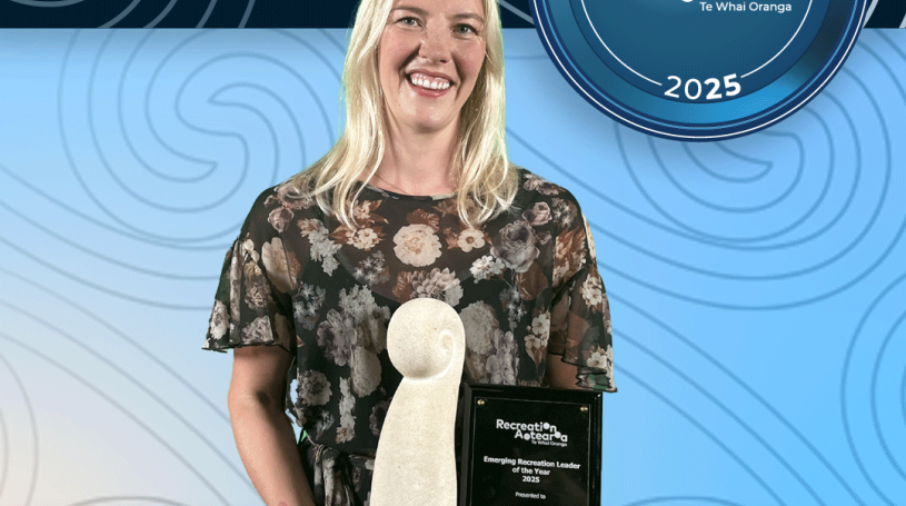 A woman standing holding a white stone koru-shaped award and smiling. The background is a blue koru pattern with text at the top and bottom of the image. The top text says "2025 Recreation Awards Winner," and the bottom says "Emerging Recreation Leader of the Year: Maria Burnett"