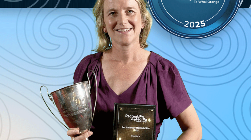 A woman standing holding a trophy cup and award plaque and smiling. The background is a blue koru pattern with text at the top and bottom of the image. The top text says "2025 Recreation Awards Winner," and the bottom says "Ian Galloway Memorial Cup: Michelle Frey"