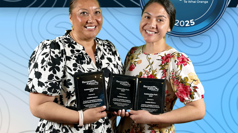 Two women standing together holding award plaques and smiling. The background is a blue koru pattern with text at the top and bottom of the image. The top text says "2025 Recreation Awards Winner," and the bottom says "Outstanding Park: Kaipātiki Reserve."