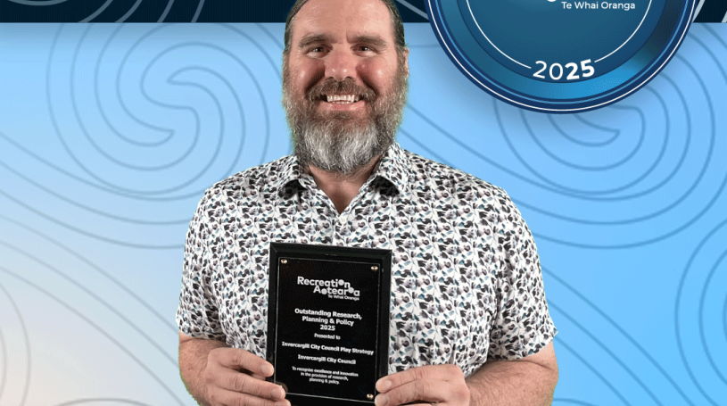 A man standing holding an award plaque and smiling. The background is a blue koru pattern with text at the top and bottom of the image. The top text says "2025 Recreation Awards Winner," and the bottom says "Outstanding Research, Policy, & Planning: Invercargill City Council Play Strategy"