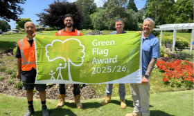 Four men hold a bright green flag in a park