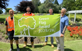 Four men hold a bright green flag in a park